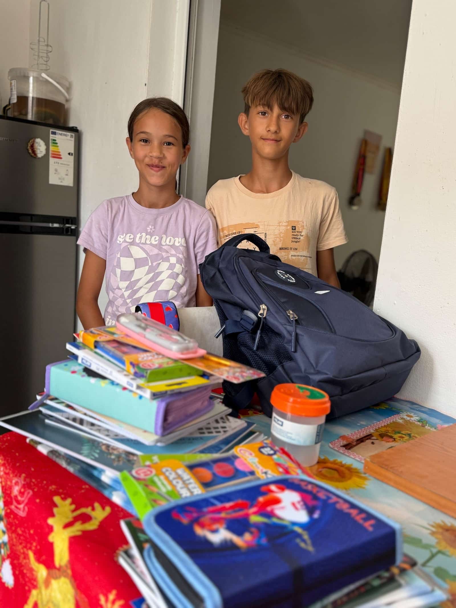 Two children beside backpacks and school supplies.