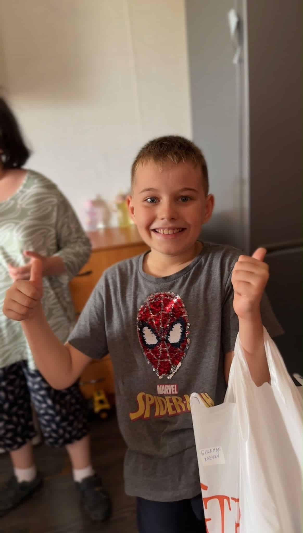 Child giving a thumbs up while holding a supply bag.