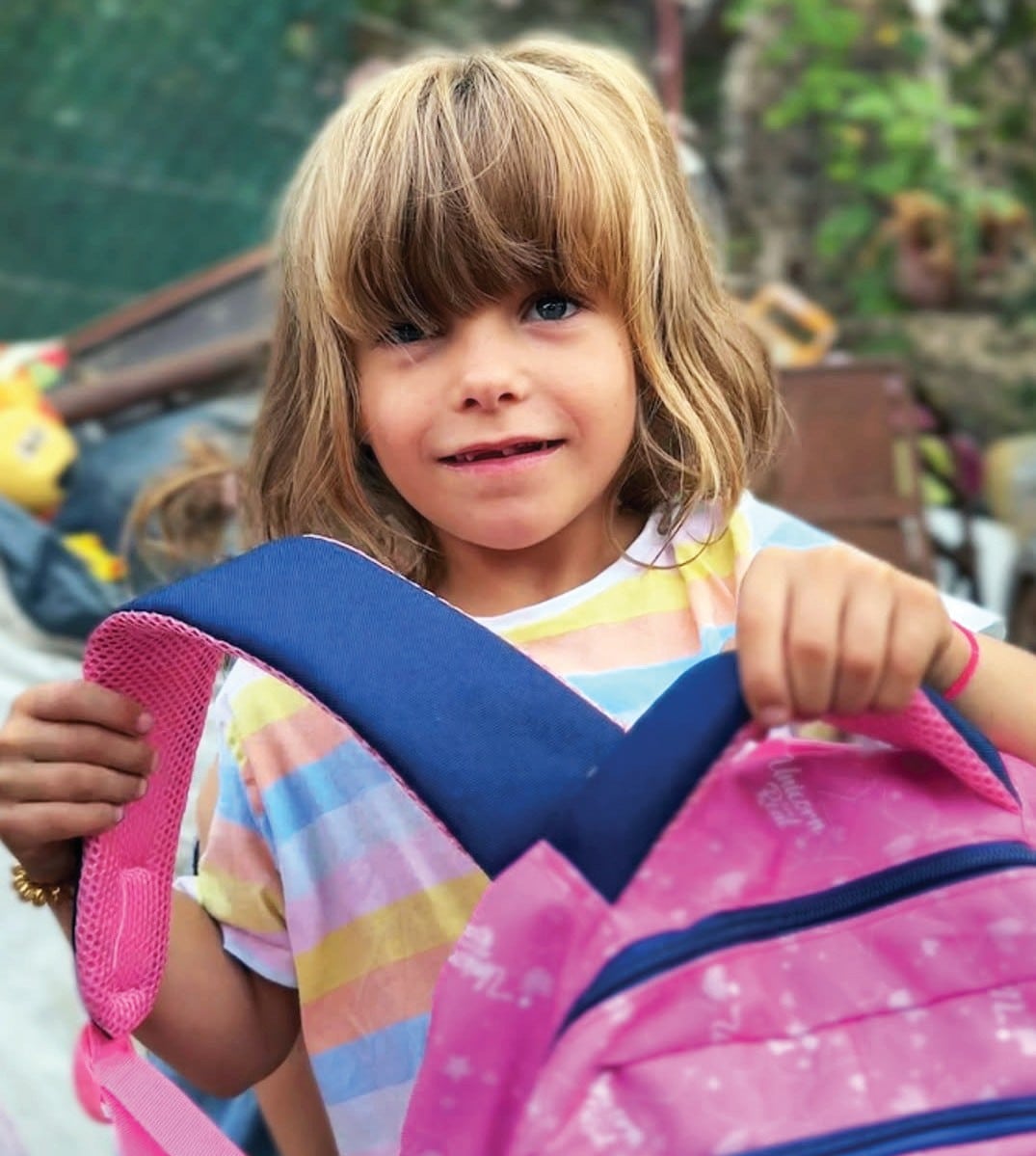 letter-backpack Child holding a colorful backpack.